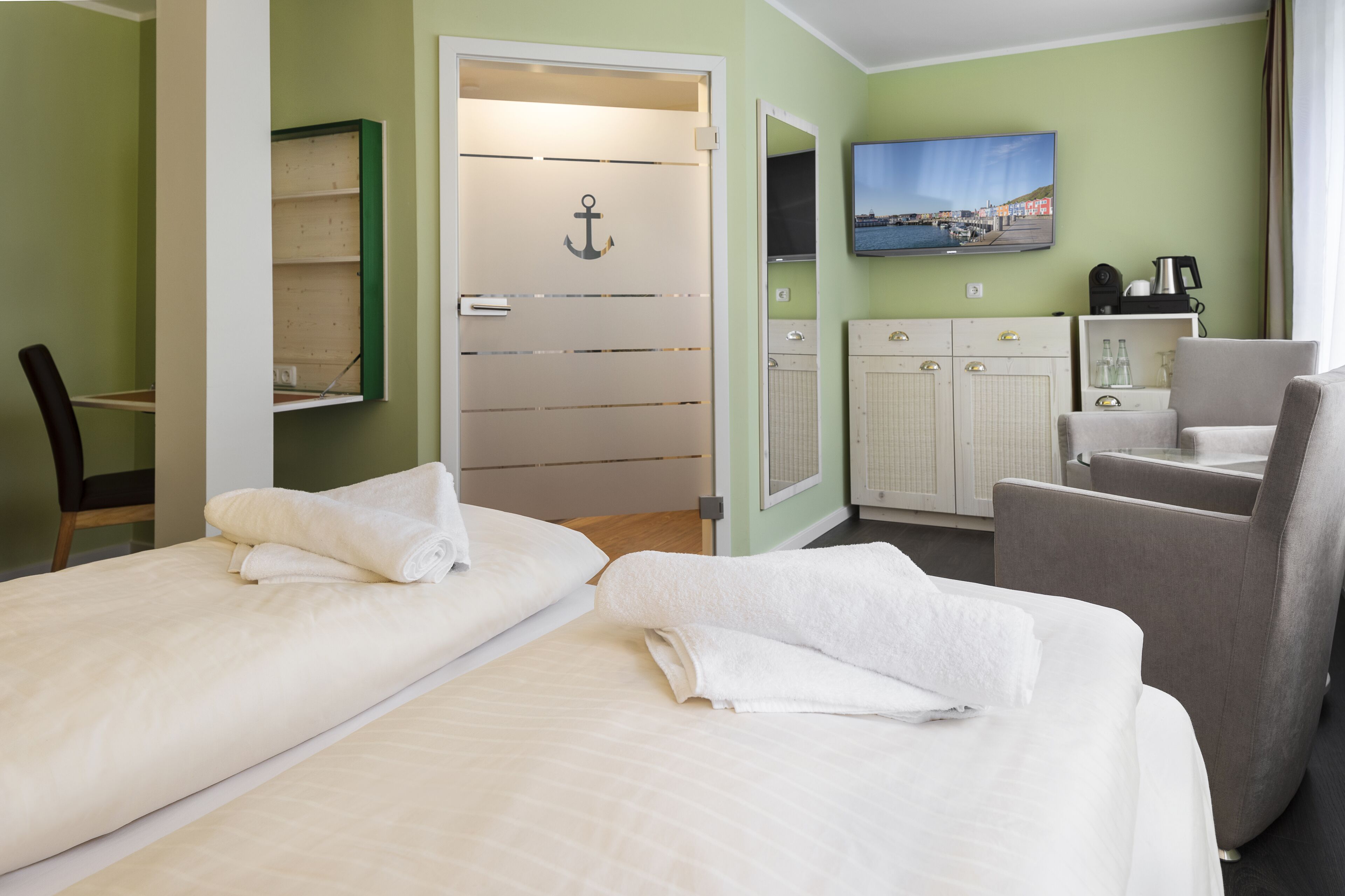 Een hotelkamer met twee bedden, een stoel, een bureau, een televisie en een schilderij aan de muur.