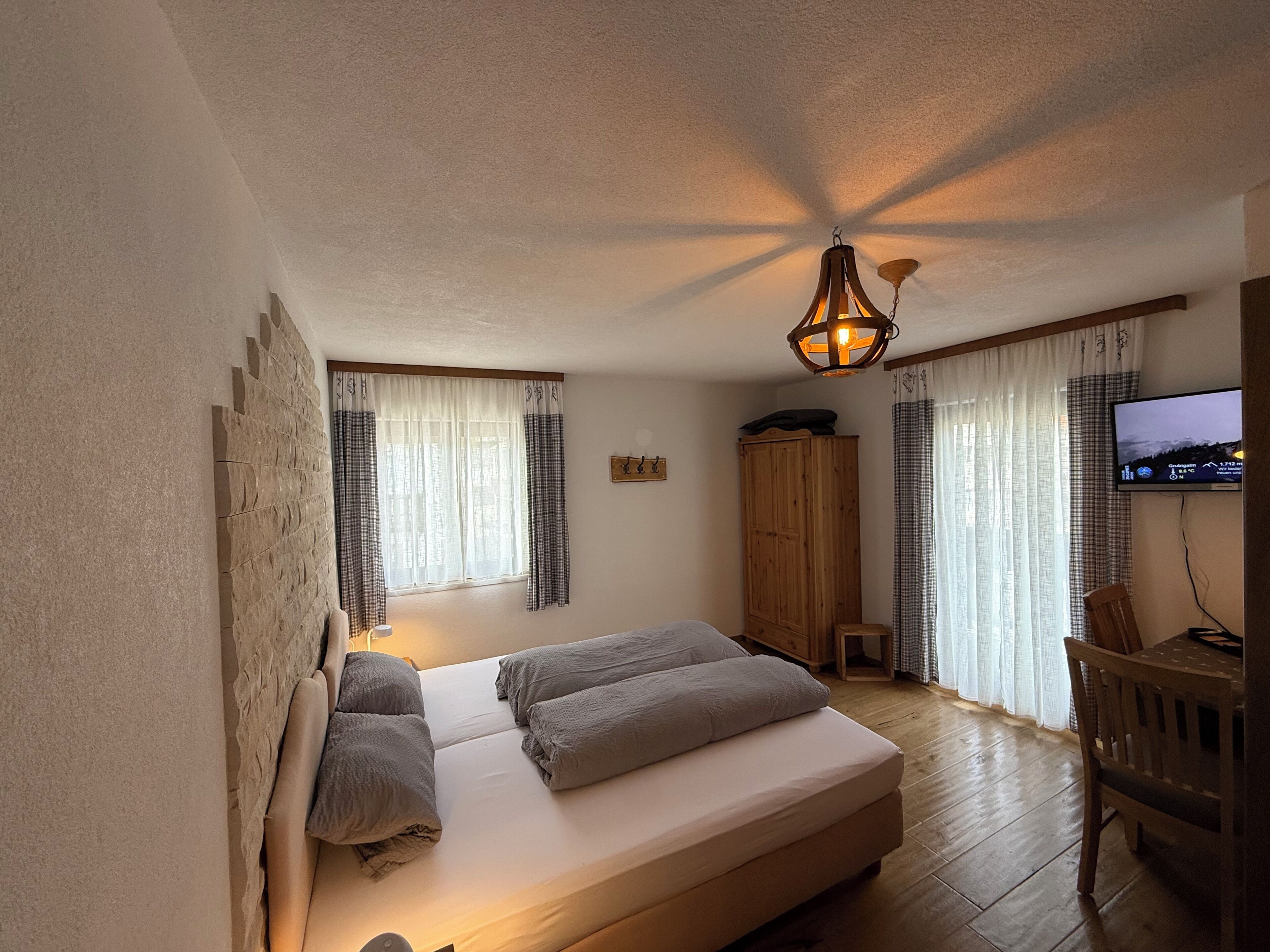Un dormitorio con cama, armario de madera, televisor y ventana con cortinas.