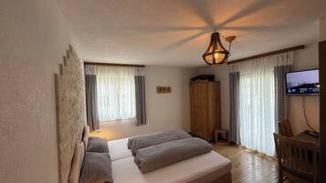 Un dormitorio con cama, armario de madera, televisor y ventana con cortinas.