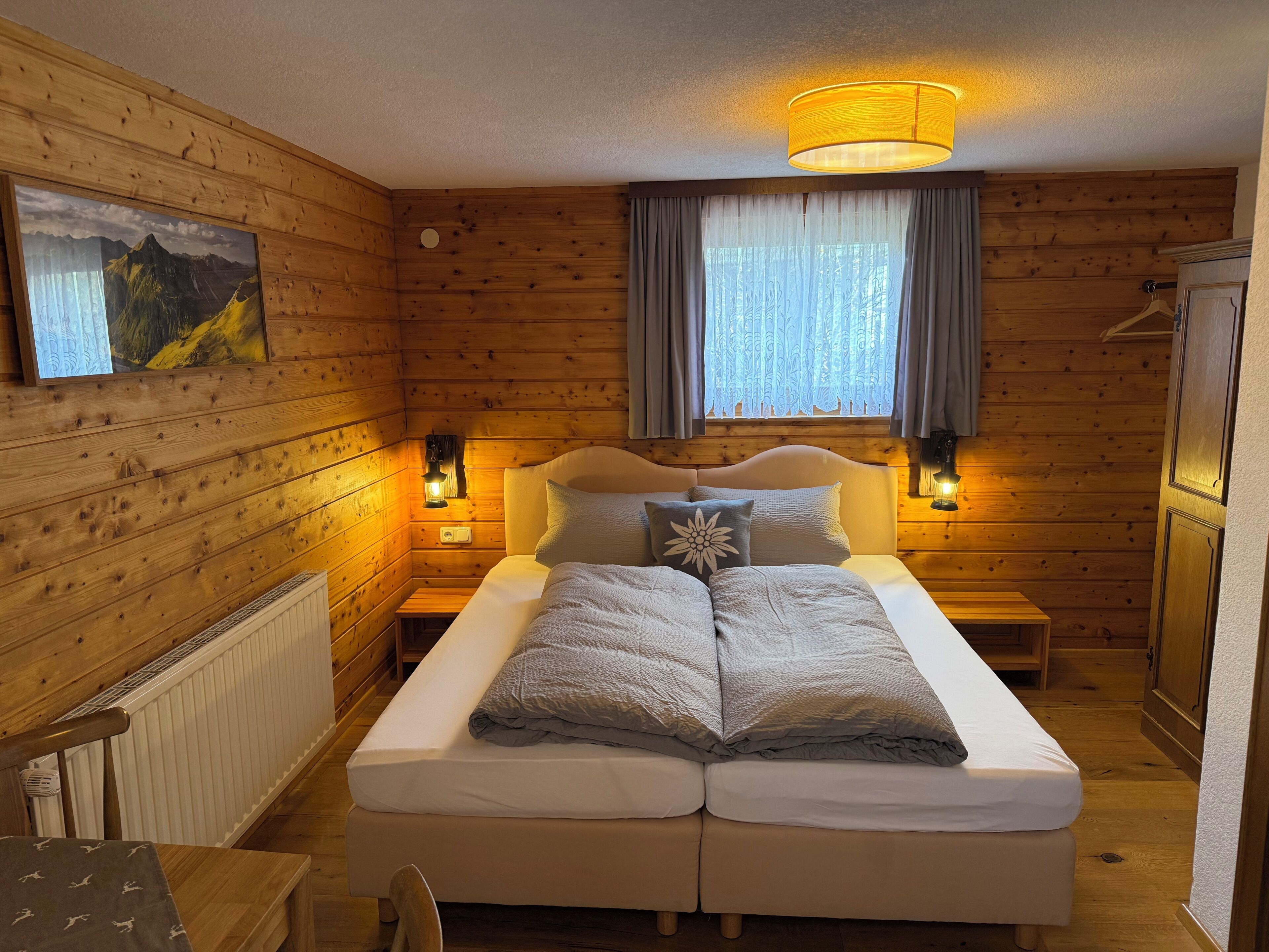A wooden-paneled room with a double bed, two bedside lamps, a radiator, and a window with curtains.