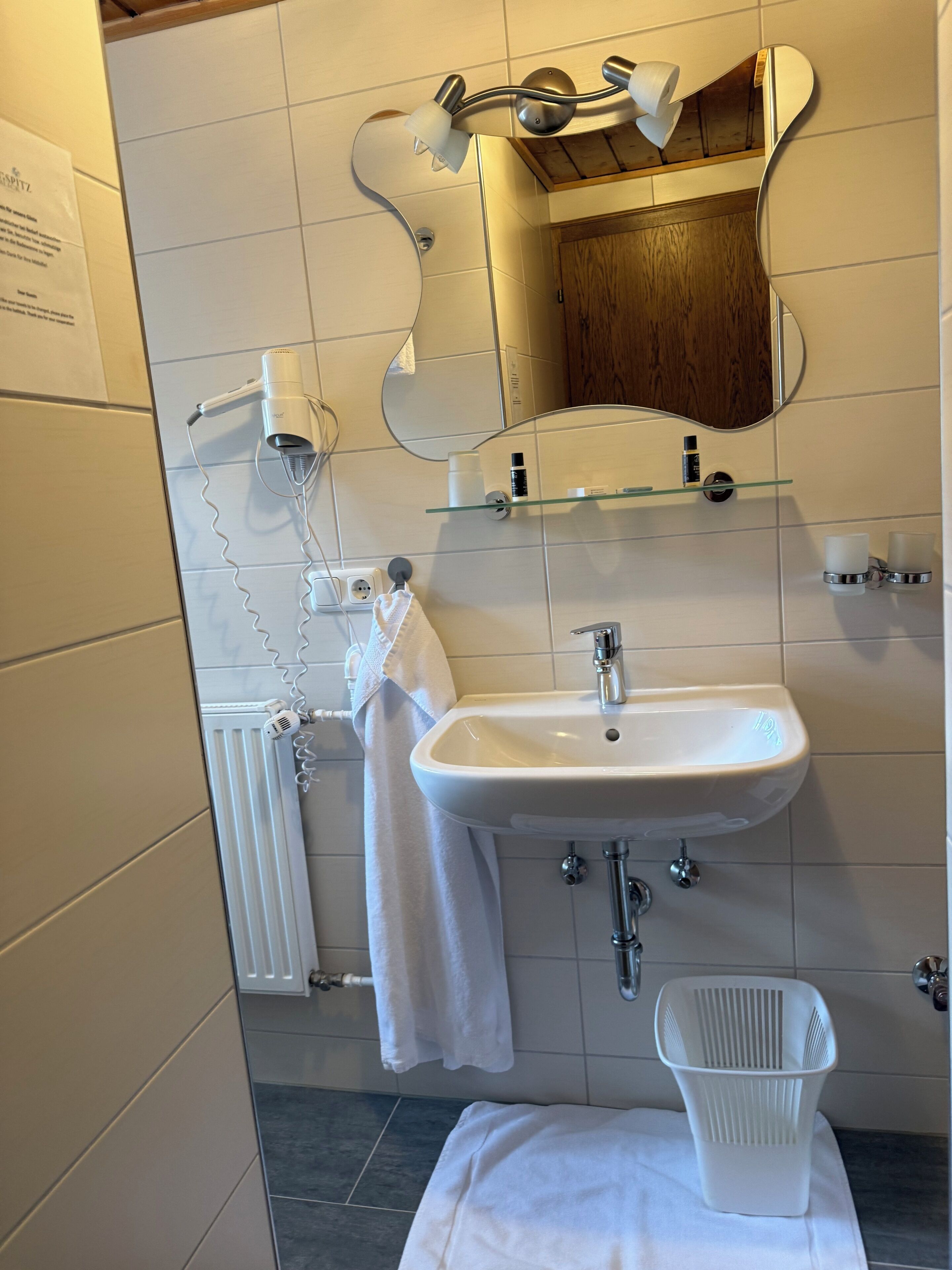 A bathroom with a white sink, mirror, towel rack, and a white basket.