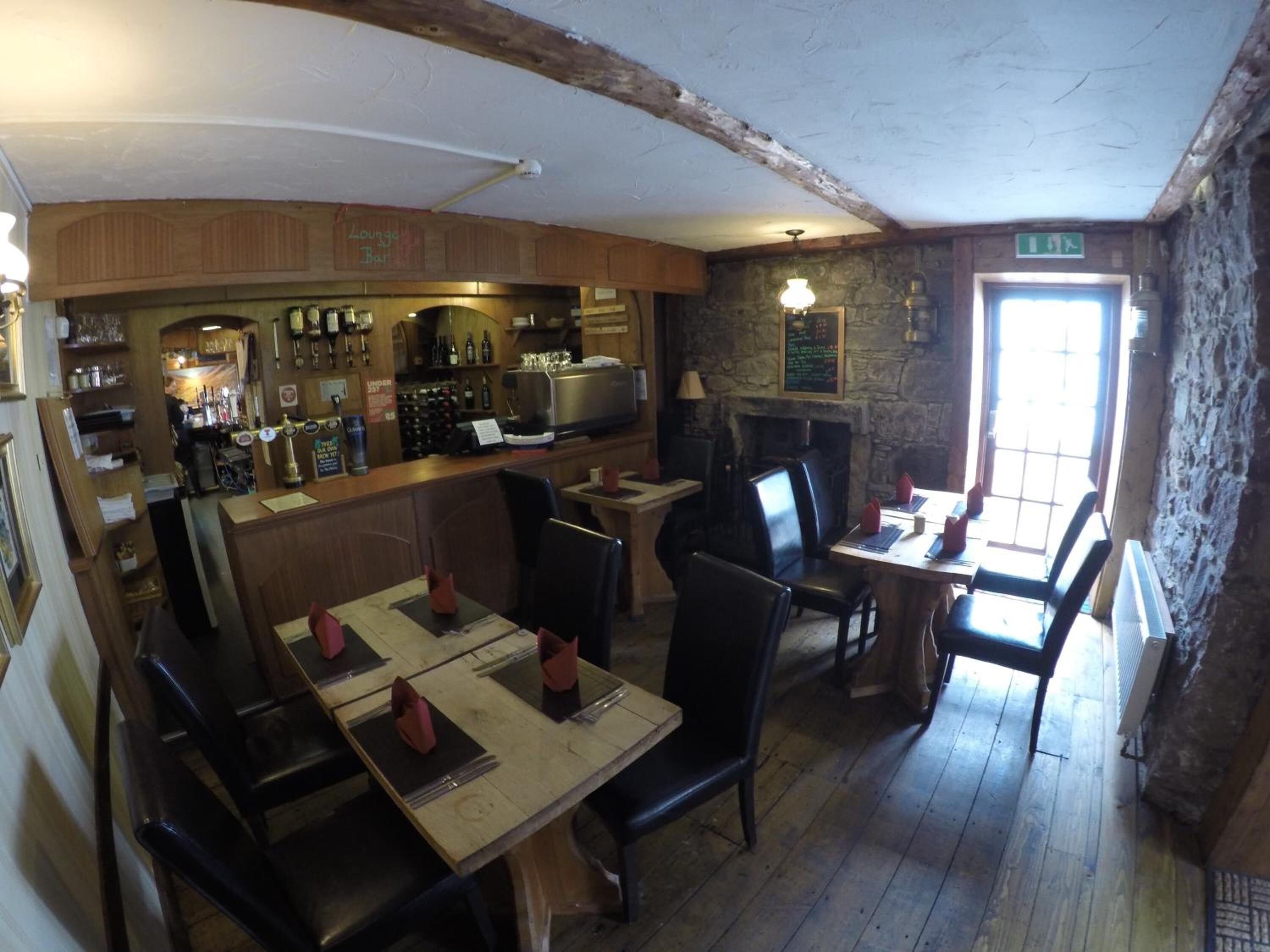 Un restaurante con mesas y sillas de madera, una zona de bar y una pared de piedra.