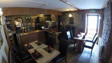 Un restaurante con mesas y sillas de madera, una zona de bar y una pared de piedra.