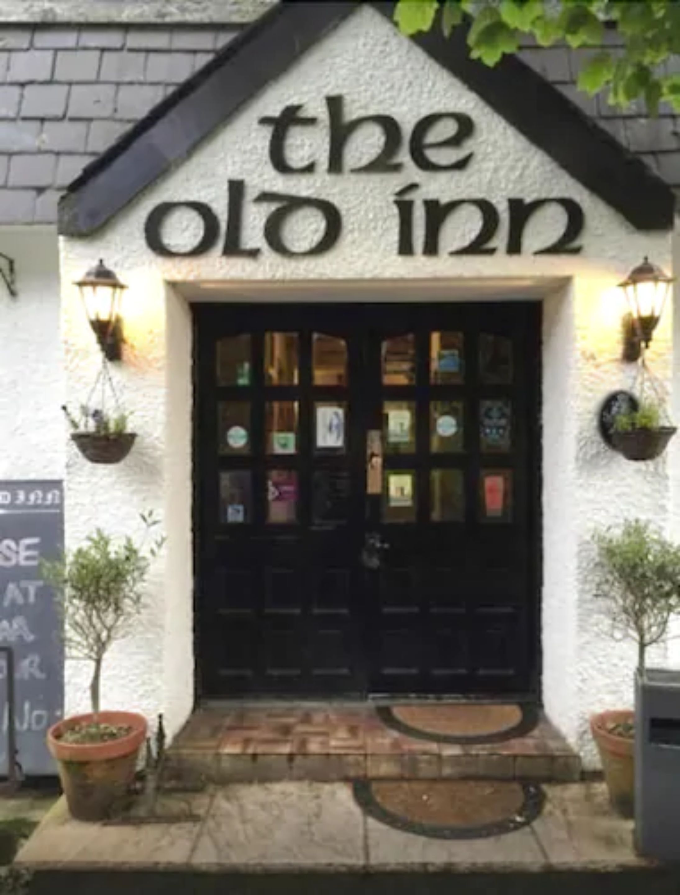 The exterior of The Old Inn with a black door, two hanging lanterns, and a signboard.