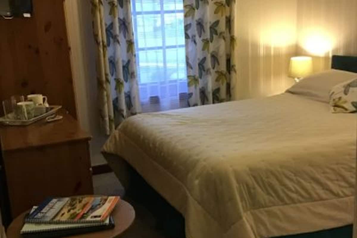 A hotel room with a bed, a bedside table with a book, a dresser, and a window with curtains.