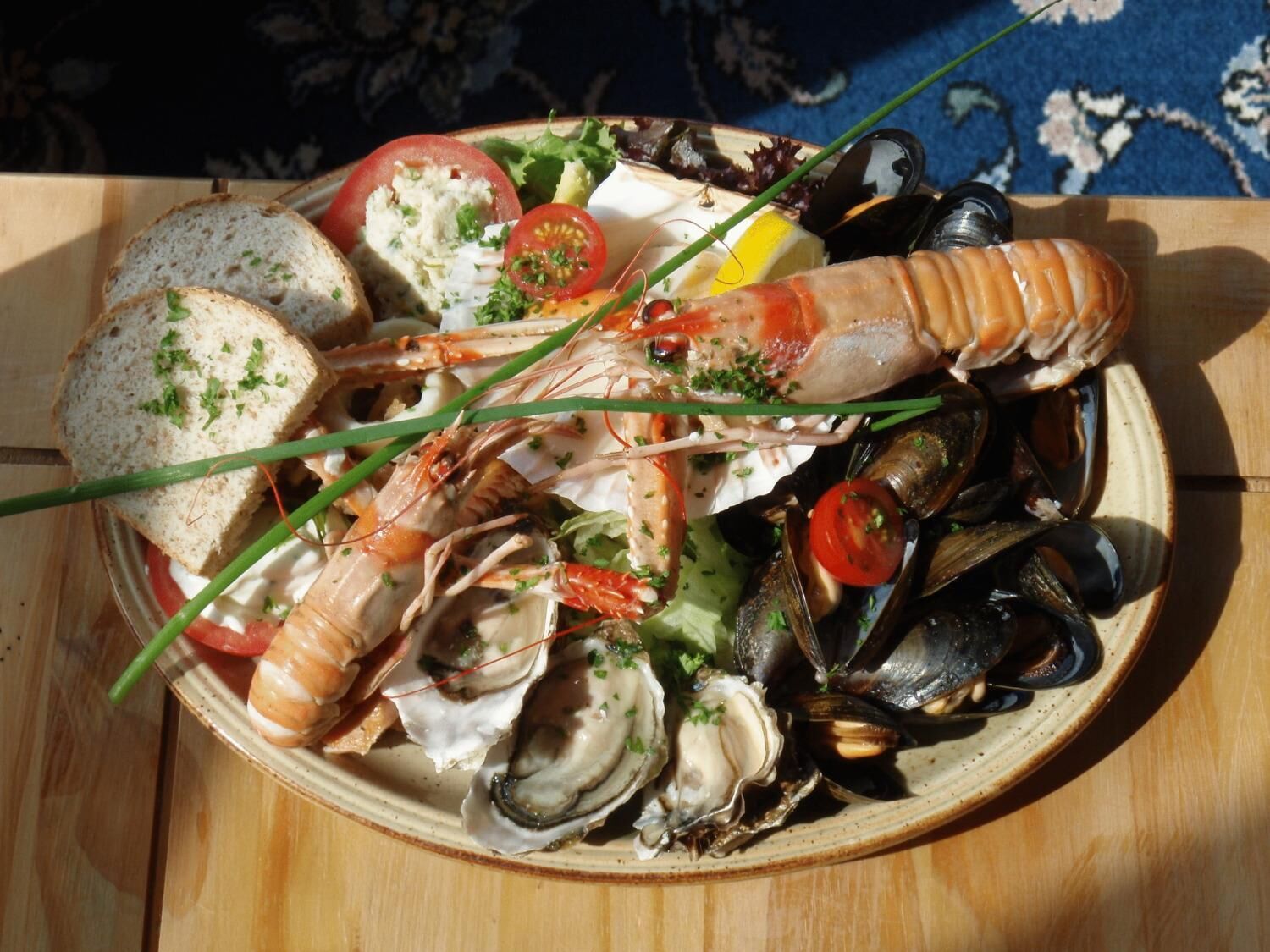 A seafood platter with shrimp, mussels, and oysters on a plate, accompanied by slices of bread and garnishes.