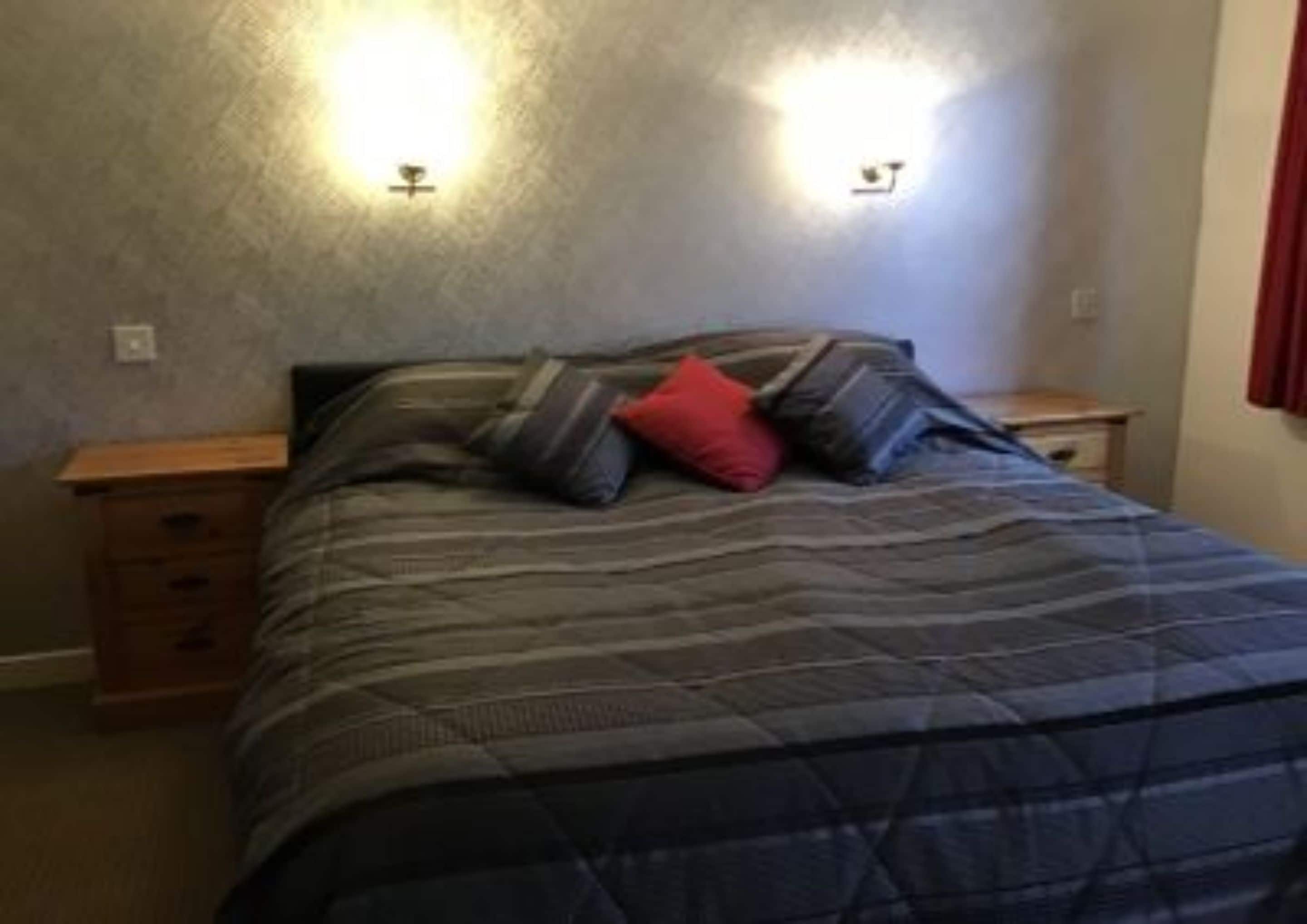 Quarto com cama, duas mesas de cabeceira e luminária na parede.
