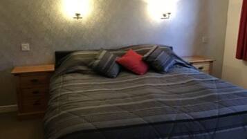 Quarto com cama, duas mesas de cabeceira e luminária na parede.