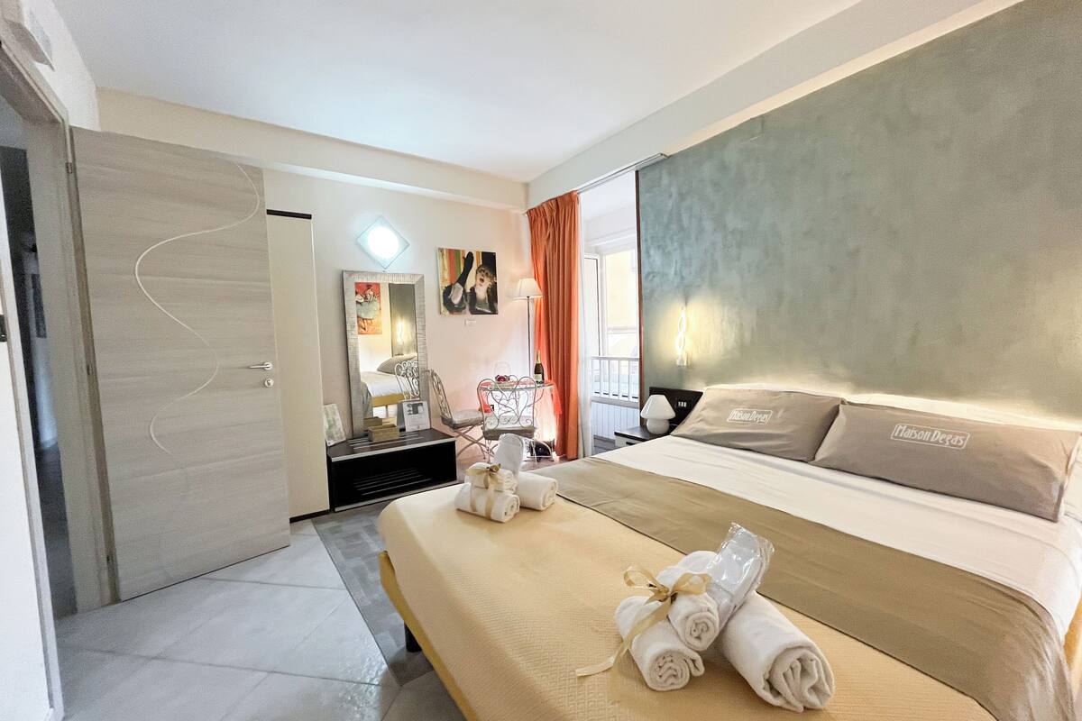 A hotel room with a bed, a desk, a chair, a mirror, and a window.