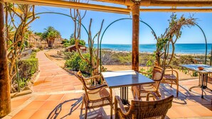 An outdoor patio with wicker furniture, a tiled floor, and a view of the beach and ocean.