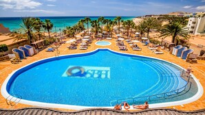 A large swimming pool with a view of the beach and ocean, surrounded by palm trees and lounge chairs. - SBH Taro Beach Hotel (Pajara)