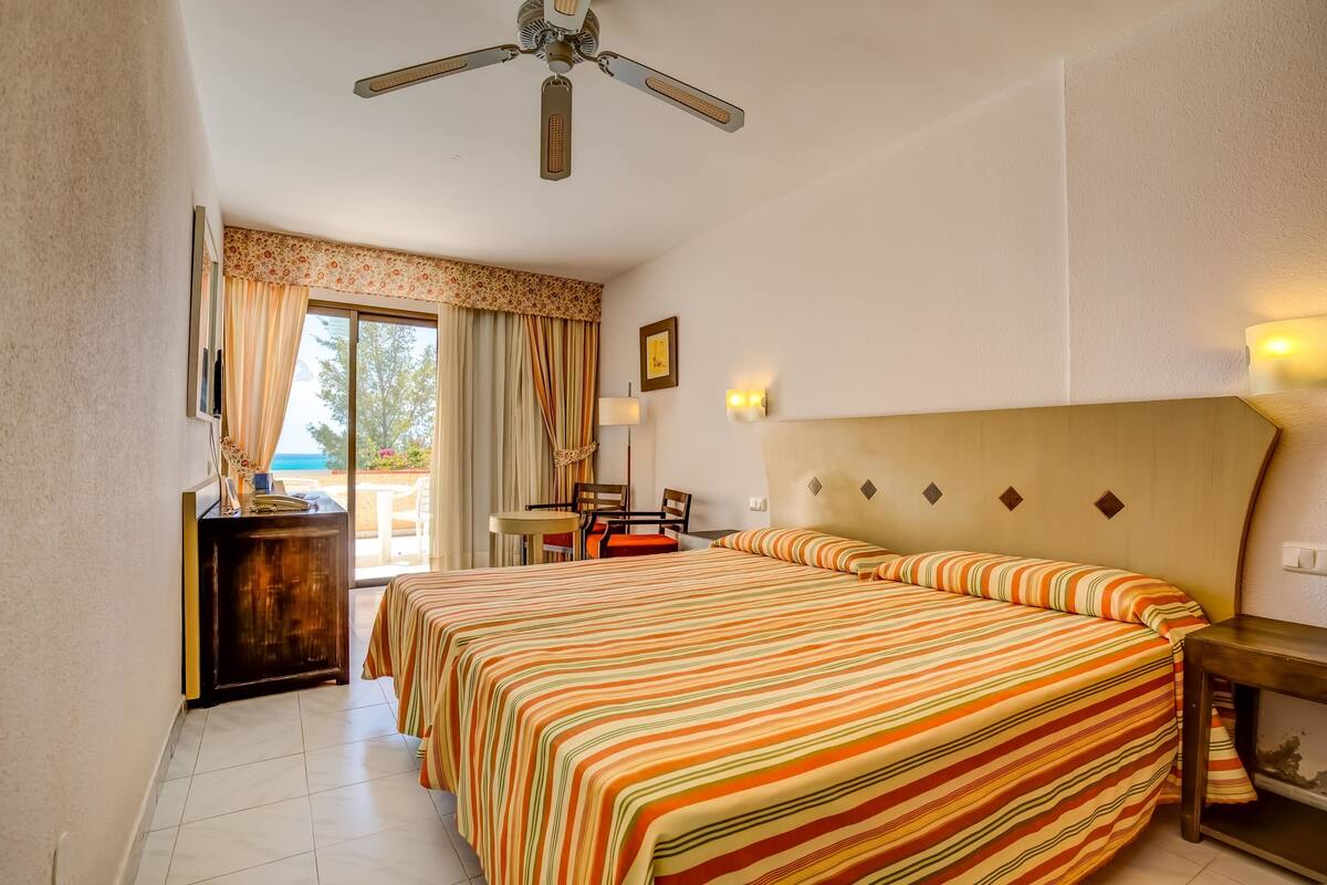 A hotel room with a large bed, a ceiling fan, a desk with a chair, and a view of the outdoors.