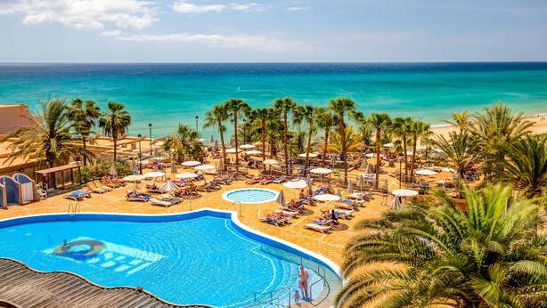 A resort with a swimming pool, beach, and palm trees.