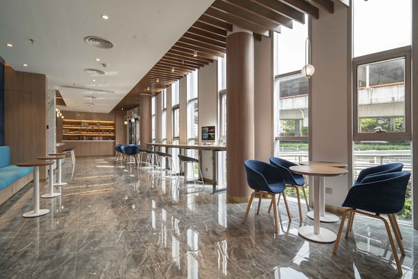 Un moderno vestíbulo de hotel con un mostrador de recepción alargado, sillas azules y un sofá azul.