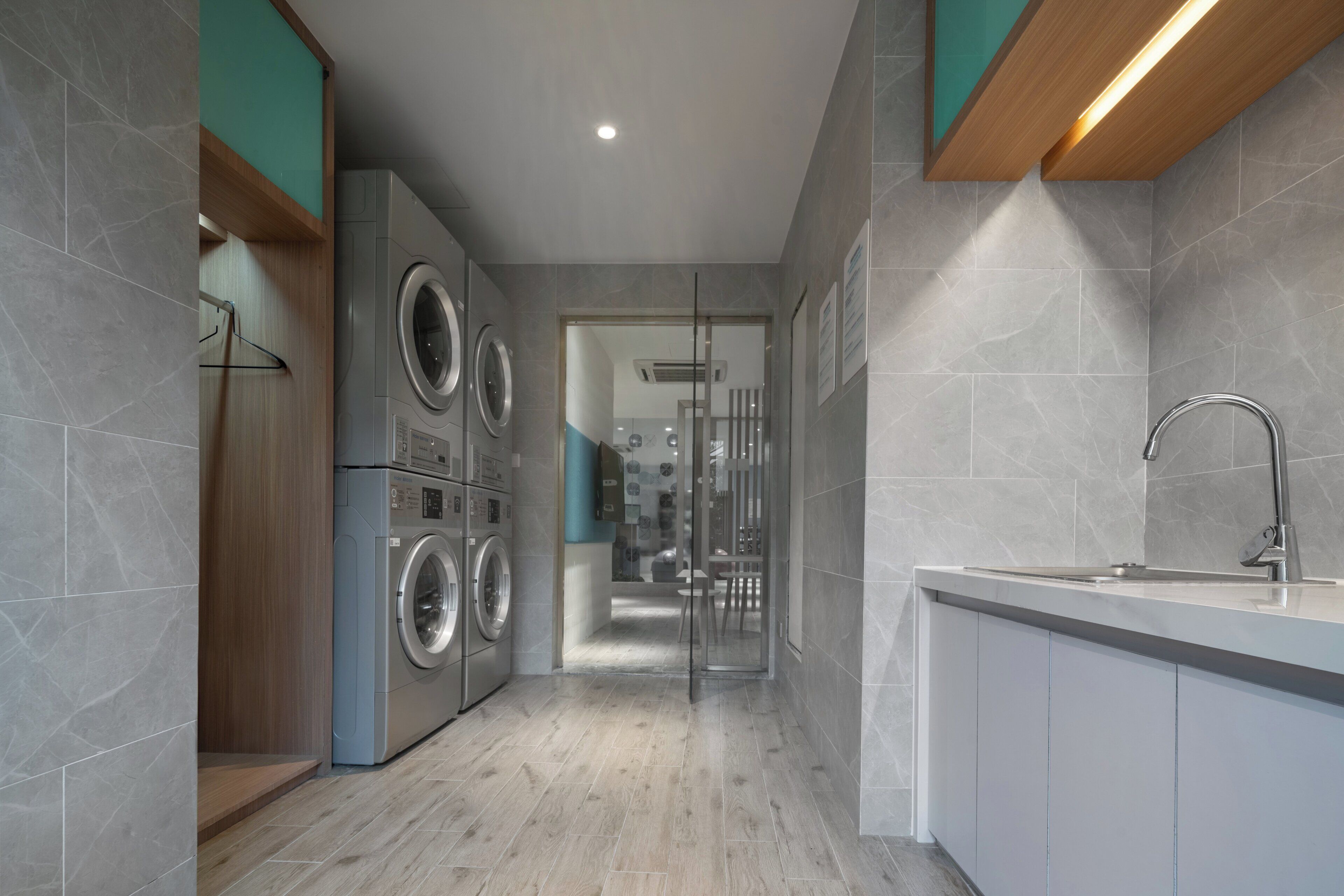 A modern kitchen with a built-in washing machine, a sink, and a glass door leading to a bathroom.