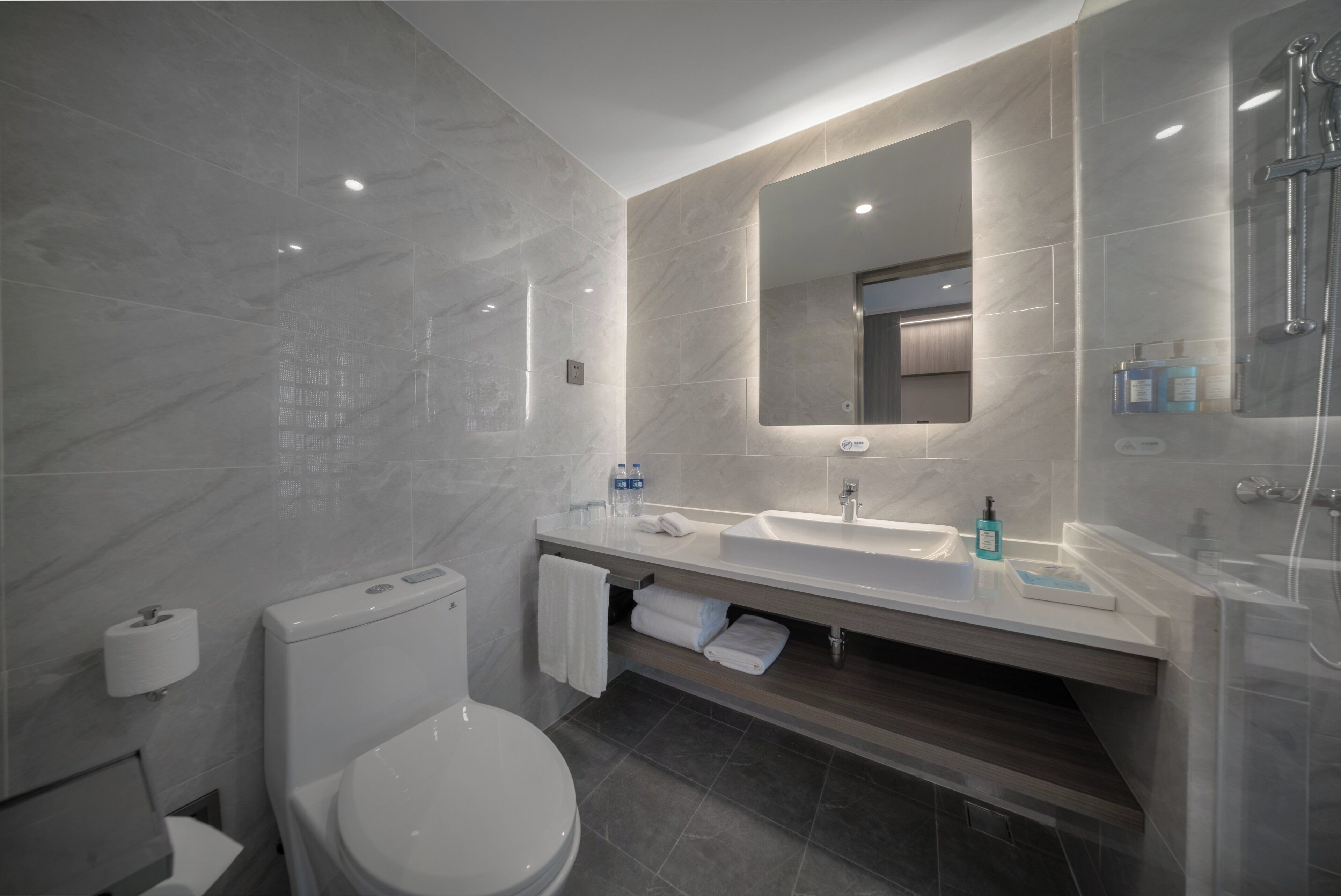 A modern bathroom with a toilet, sink, mirror, and shower.