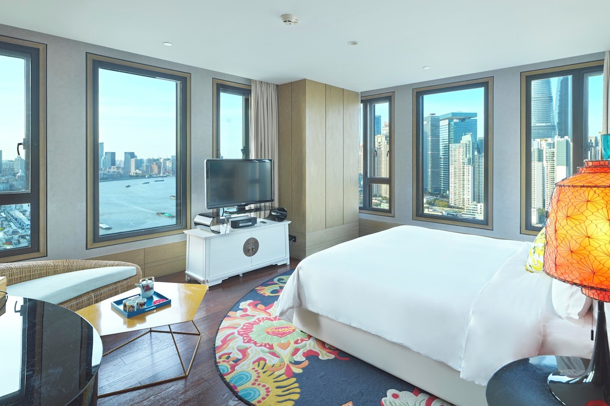 Une chambre d’hôtel avec un grand lit, une télévision, un bureau et une vue sur la ville et l’eau.