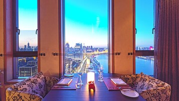 A dining area with a table set for two, large windows with a cityscape view, and a decorative candle on the table.