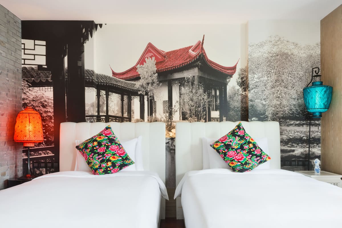 Une chambre d’hôtel avec deux lits, une fresque représentant une architecture traditionnelle et une lanterne rouge.