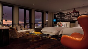 A hotel room with a city view, a sofa, two beds, a coffee table, and a chair.