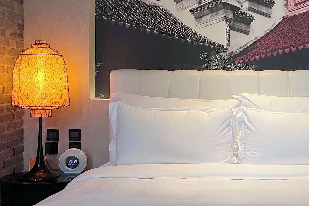 Une chambre d’hôtel avec un lit, une horloge fixée au mur et une lampe décorative.