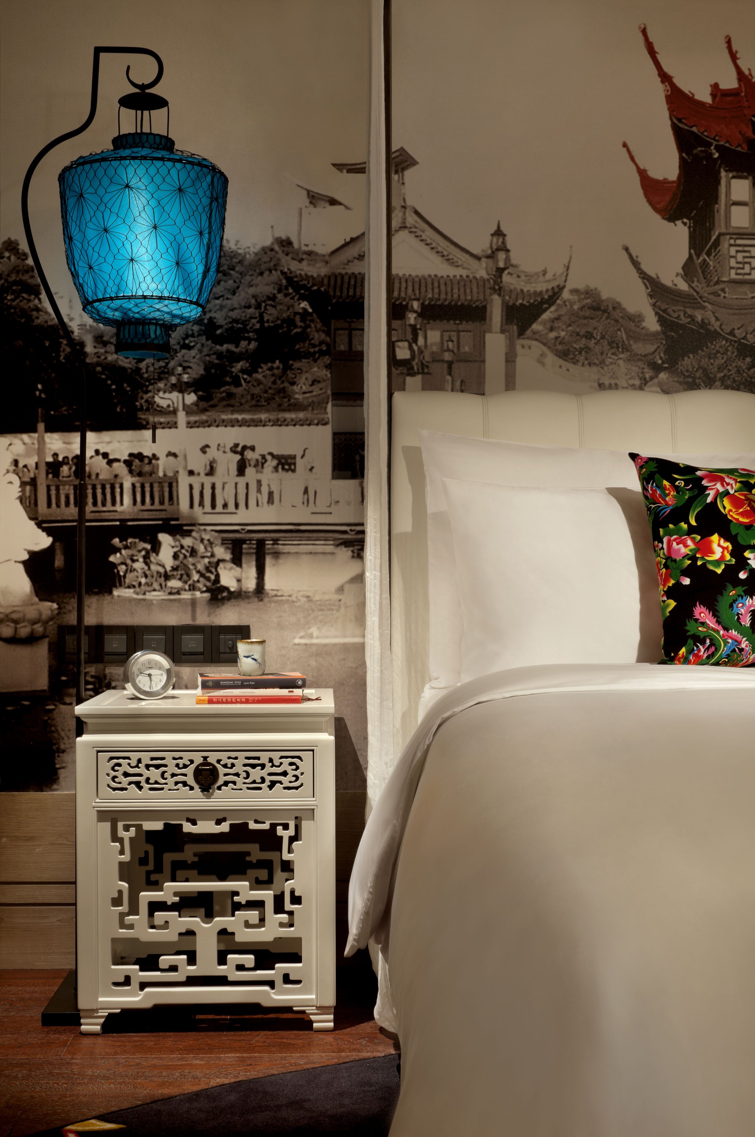 Un dormitorio con una lámpara de estilo asiático tradicional, una mesita de noche decorativa y un mural de una edificación tradicional.