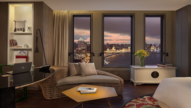 Habitación de hotel con vista a la ciudad, un escritorio con una computadora portátil, un sofá y una mesita con libros.