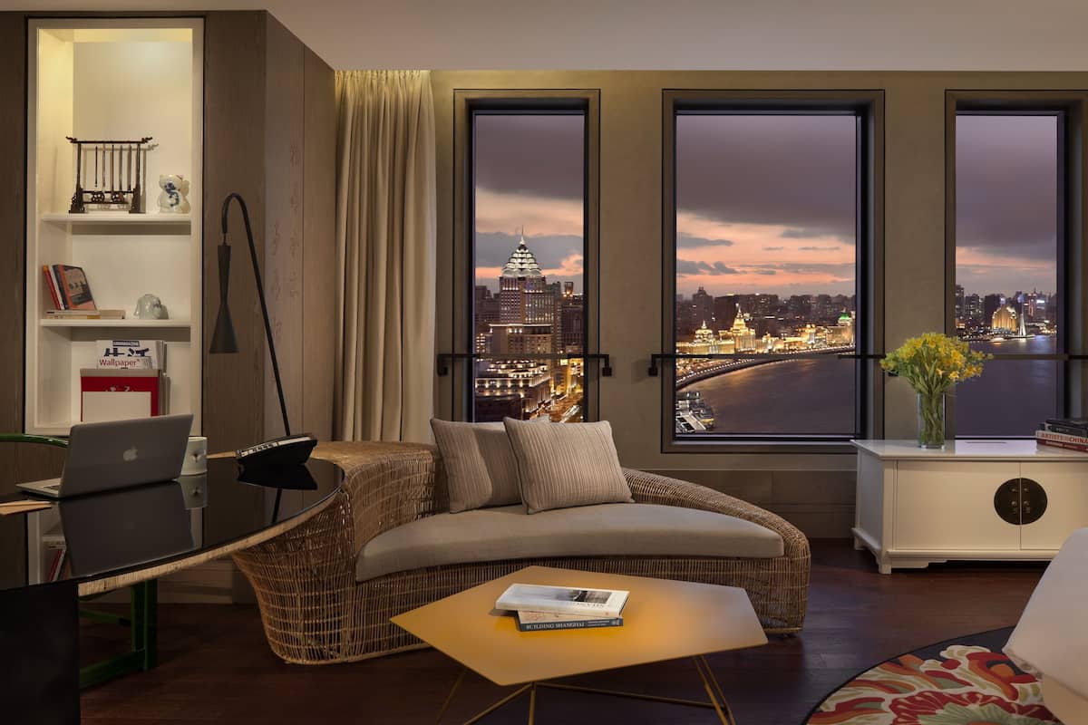 Une chambre d’hôtel avec vue sur la ville, un bureau avec un ordinateur portable, un canapé et une petite table avec des livres.
