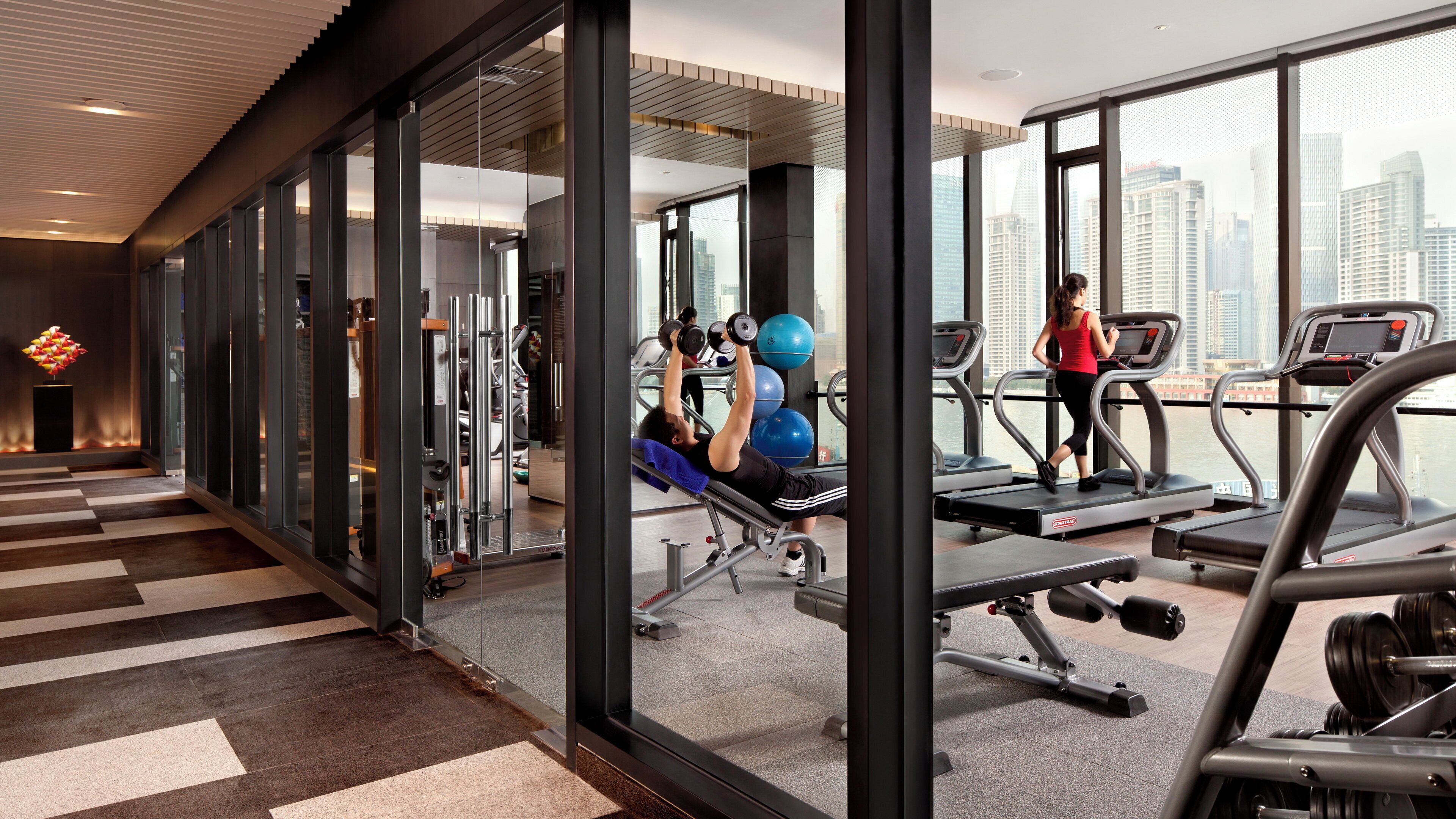Un gimnasio con equipo de ejercicio, cinta de correr y vistas a la ciudad.