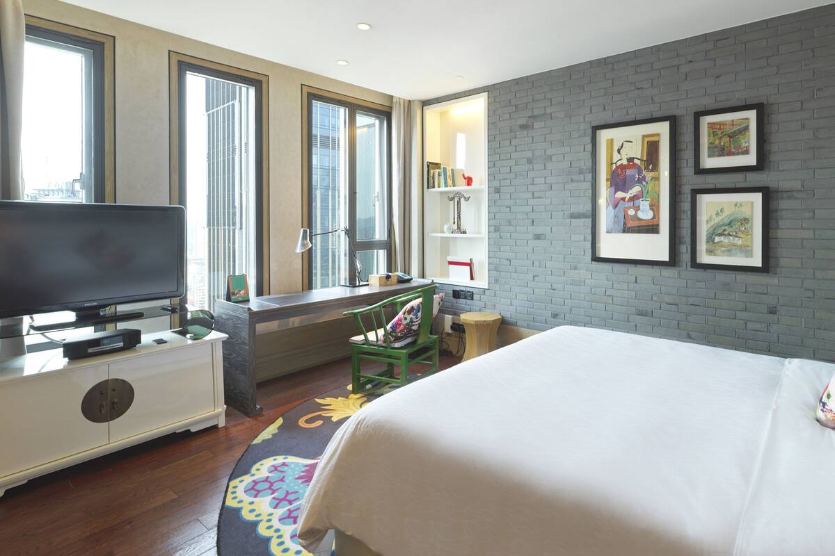 Une chambre d’hôtel comprenant un lit, un bureau avec un ordinateur, une télévision et une bibliothèque.