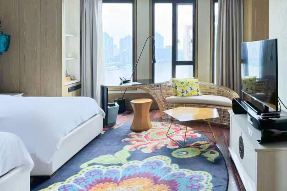 Une chambre d’hôtel équipée d’un lit, d’un canapé, d’une télévision, d’un bureau et offrant une vue sur la ville grâce à de grandes fenêtres.