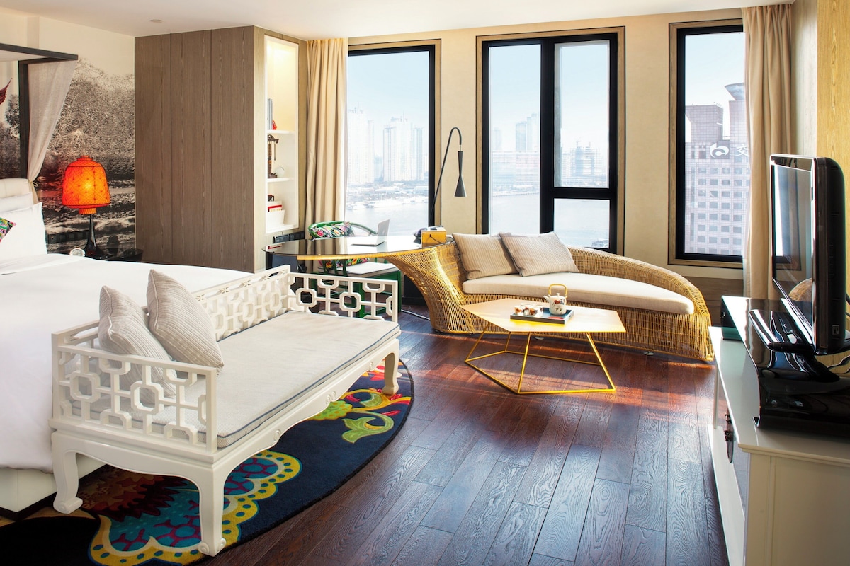 Une chambre d’hôtel avec un lit, un canapé, une chaise, une télévision et une vue sur la ville.