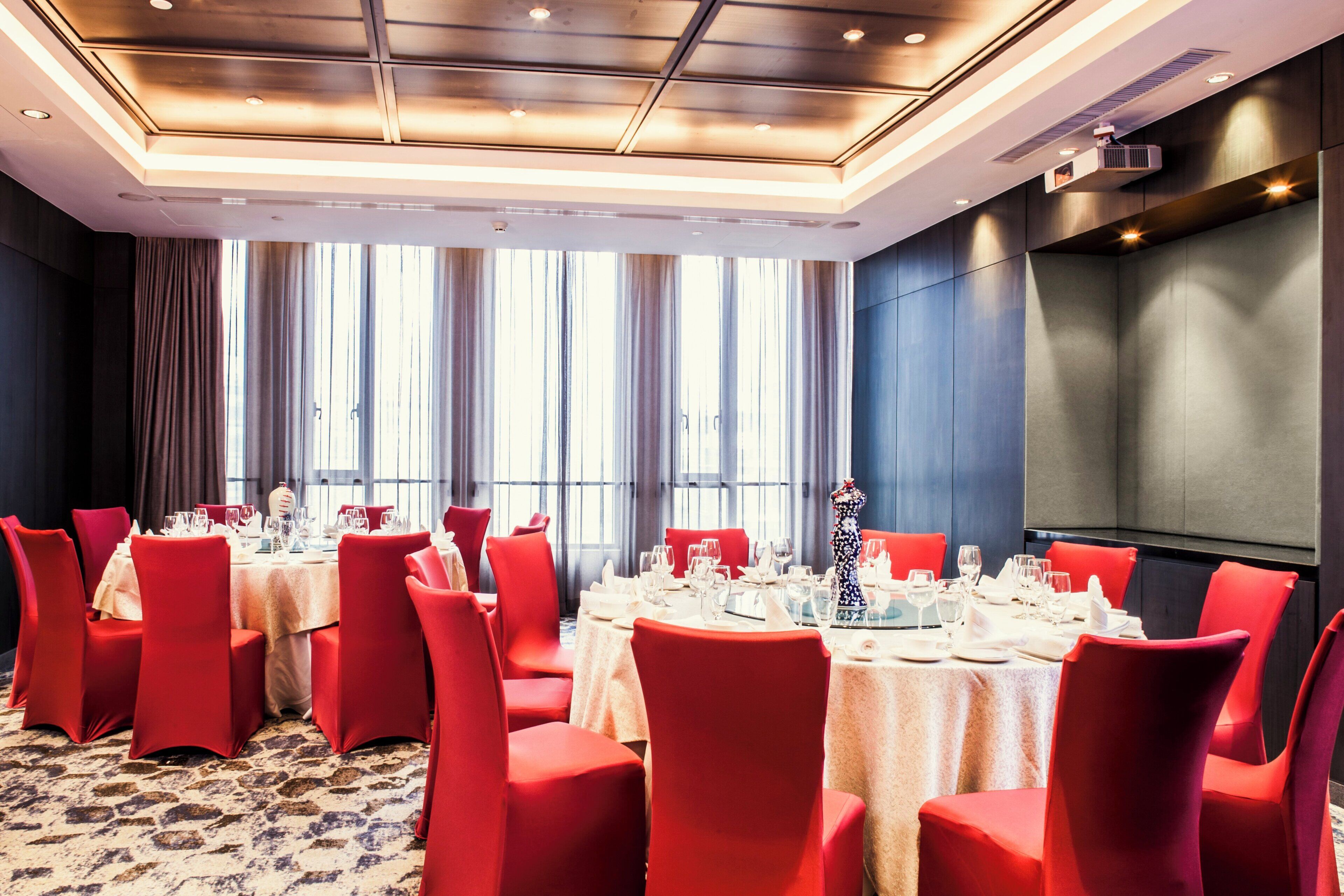 A conference room with a long table set for a meeting, surrounded by red chairs, large windows, and a modern ceiling design.