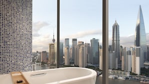 Ein modernes Badezimmer mit einer großen Badewanne, einem hölzernen Tablett und Blick auf eine Stadtlandschaft mit hohen Gebäuden und einem Fluss.