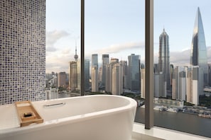 Une salle de bain moderne avec une grande baignoire, un plateau en bois et une vue sur les gratte-ciel d’une ville, ainsi que sur une rivière.