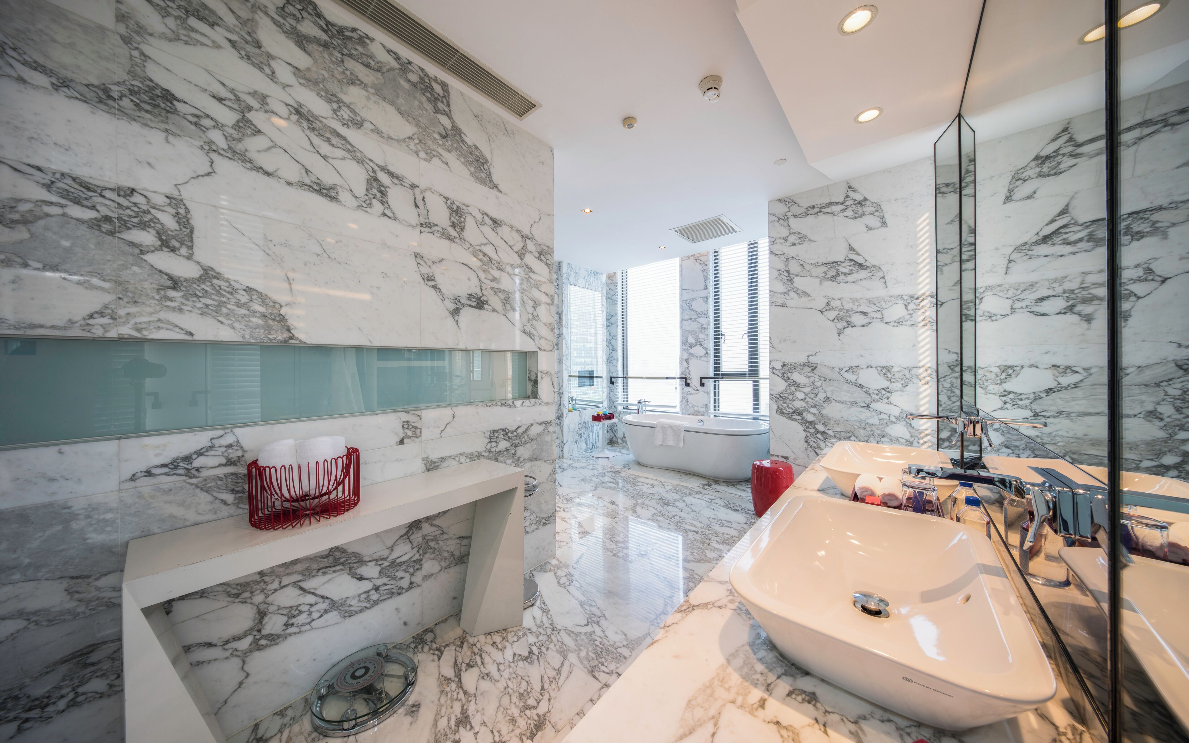 A modern bathroom with marble walls, a large bathtub, and a glass shower enclosure.