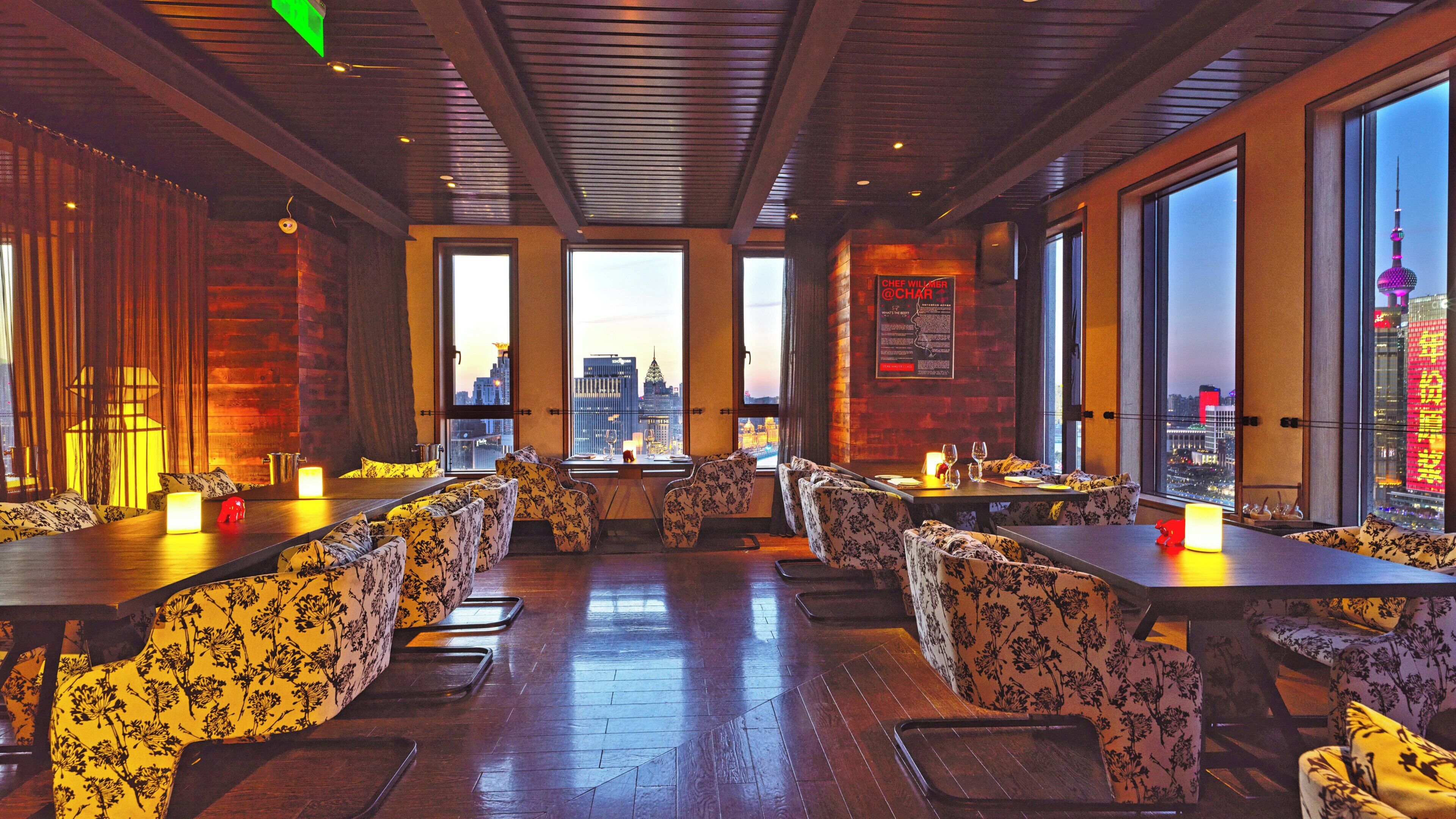 A restaurant with high ceilings, large windows, and a city view.