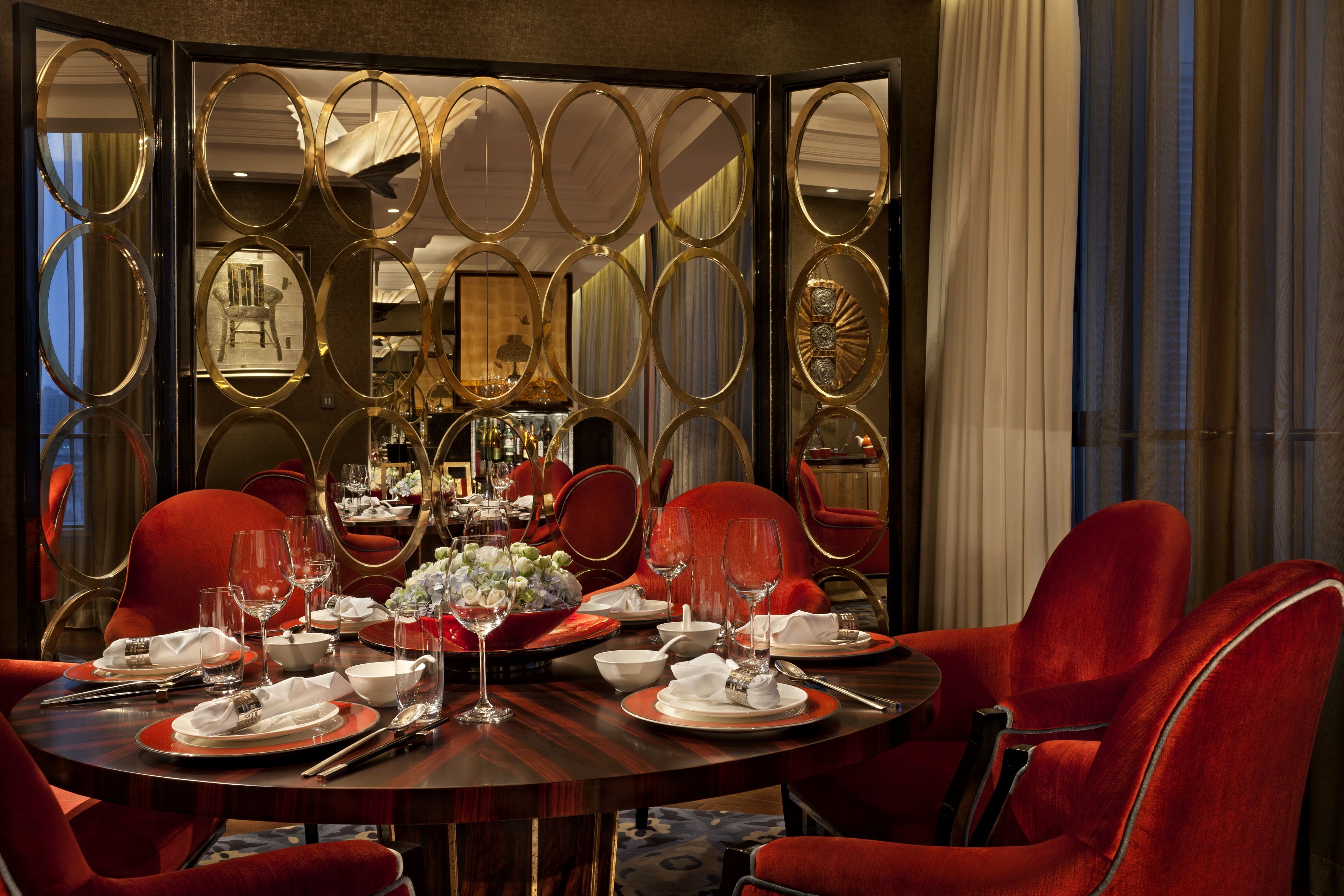 Comedor con una mesa redonda dispuesta para seis personas, rodeada de sillas tapizadas en rojo.