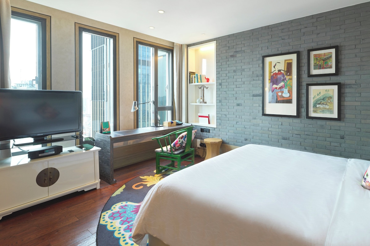 Une chambre d’hôtel avec un lit, un bureau avec un ordinateur, une télévision et une fenêtre avec des rideaux.