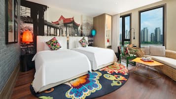 A hotel room with two beds, a sofa, a small table, a colorful rug, and a city view.