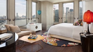 Una habitación de hotel moderna con una cama grande, un sofá, una mesita y vistas a la ciudad a través de amplios ventanales.