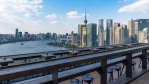 Un horizonte urbano con edificios modernos, un río y vistas desde una terraza de madera con sillas.