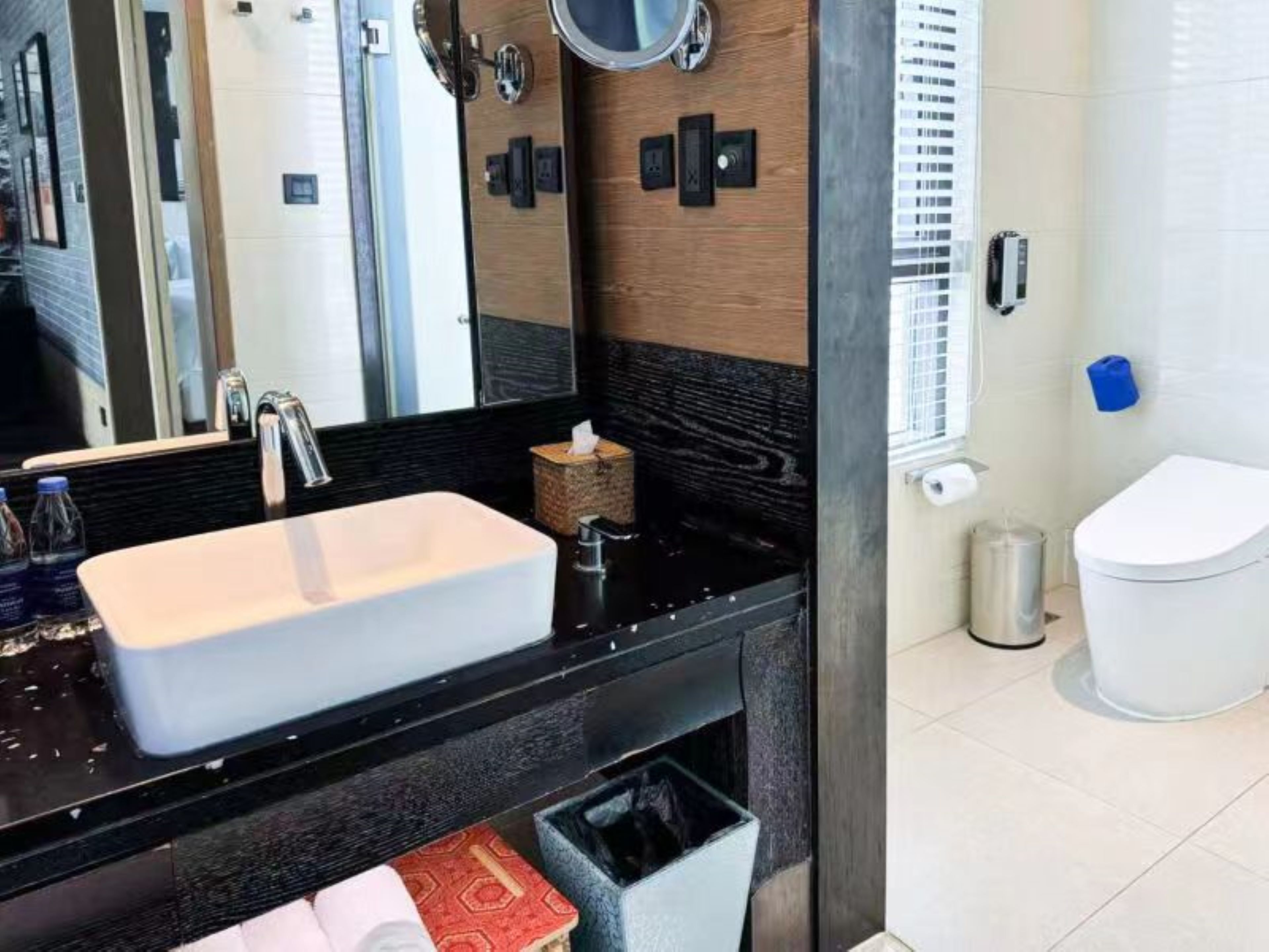 Un baño moderno con un espejo grande, un lavabo rectangular, un dispensador de toallas y un inodoro.