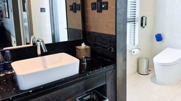 Un baño moderno con un espejo grande, un lavabo rectangular, un dispensador de toallas y un inodoro.
