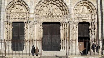 A Gothic-style cathedral with three large arched doorways, each adorned with intricate stone carvings and statues.
