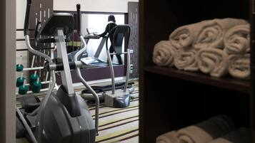 Une salle de sport équipée de matériel d’exercice, d’un tapis de course et de serviettes rangées sur des étagères.