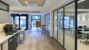 A modern office space with a kitchen area, meeting room, and large windows offering views of the outdoors. - Mercure Chartres Centre Cathédrale (Chartres)