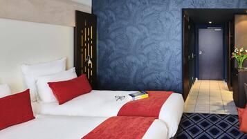A hotel room with two beds, a blue leaf-patterned wall, a dark door, and a tiled floor.