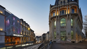 A historic building with a prominent tower and large windows, adjacent to a modern hotel with a visible entrance and signage. - Mercure Chartres Centre Cathédrale (Chartres)