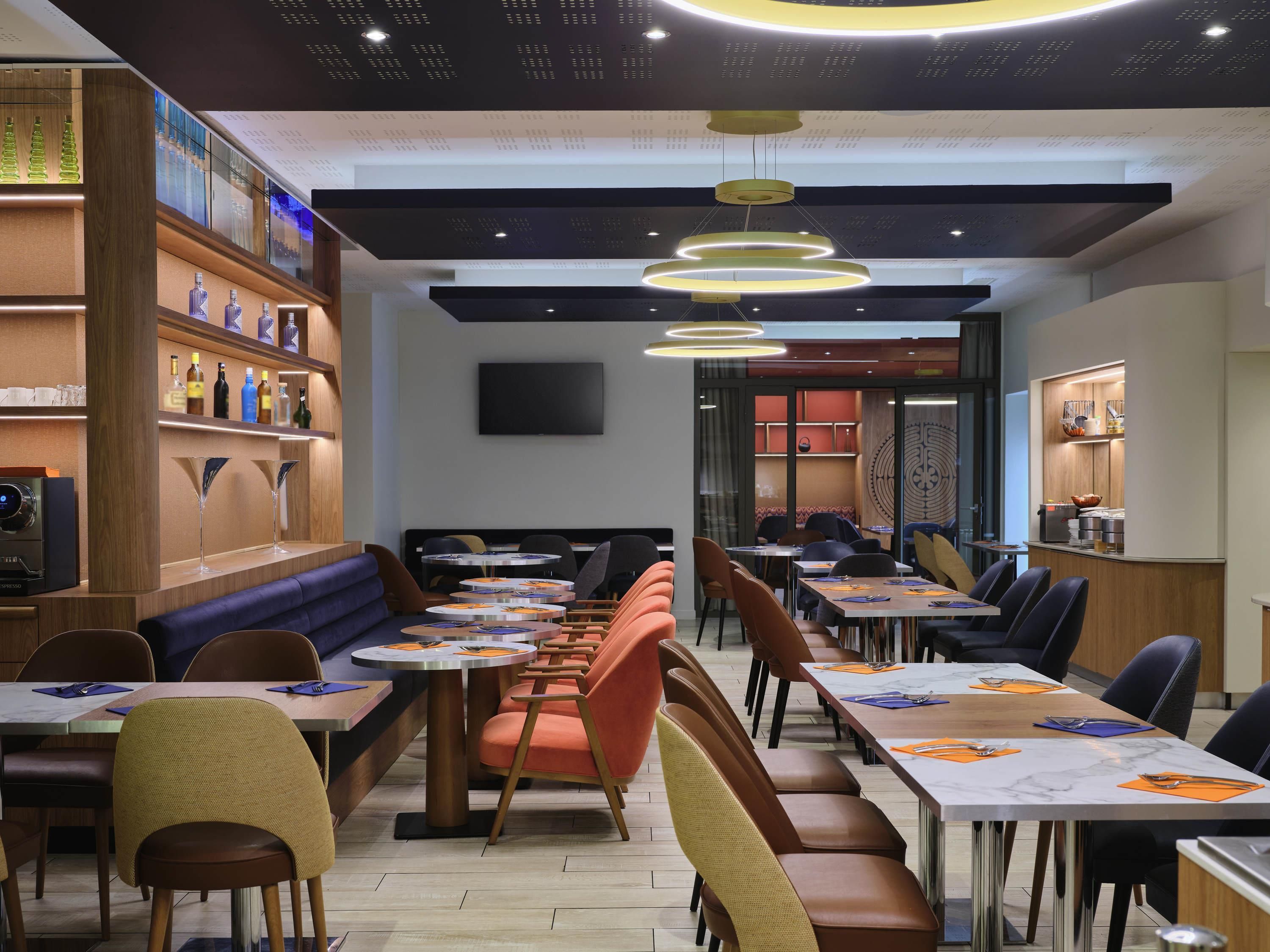 A modern restaurant interior with round tables, cushioned booths, and a bar area.